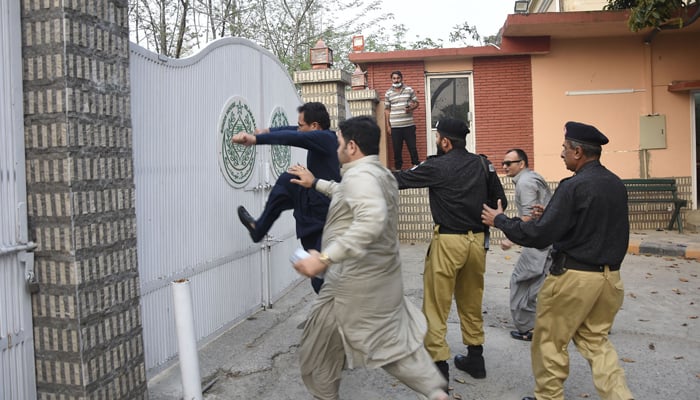 PTI member kicking Sindh Houses gate as the police try to stop him. — ONLINE