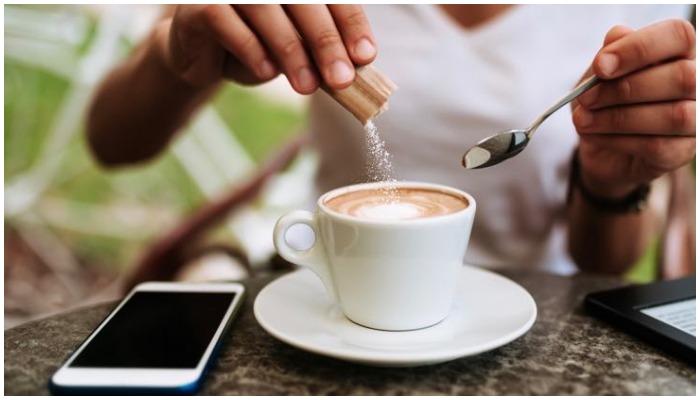 Gambar menunjukkan seseorang menuangkan pemanis buatan ke dalam kopinya.  — Askthescientists.com