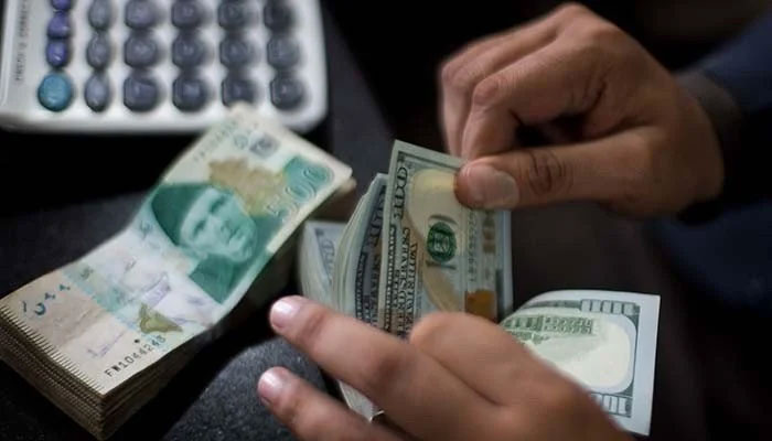 A currency dealer can be seen counting $100 notes while a stack of Rs500 notes is placed on the table. — AFP/File