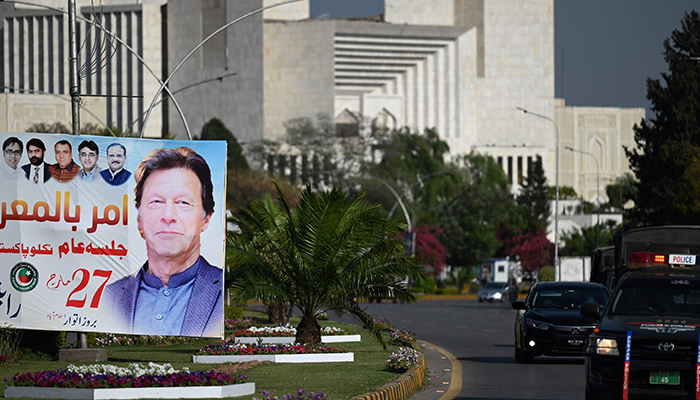 31 مارچ 2022 کو اسلام آباد میں پارلیمنٹ کی عمارت کے قریب گاڑی والے وزیر اعظم عمران خان کی تصویر والا بینر پاس کر رہے ہیں۔  - اے ایف پی