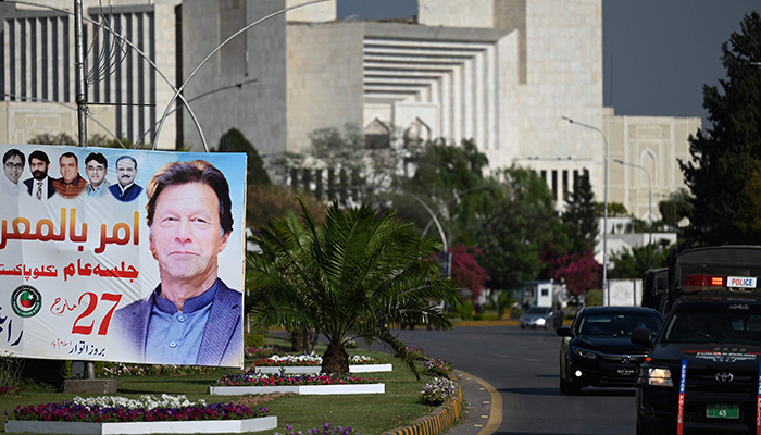 31 مارچ 2022 کو اسلام آباد میں پارلیمنٹ کی عمارت کے قریب گاڑی والے وزیر اعظم عمران خان کی تصویر والا بینر پاس کر رہے ہیں۔ - اے ایف پی