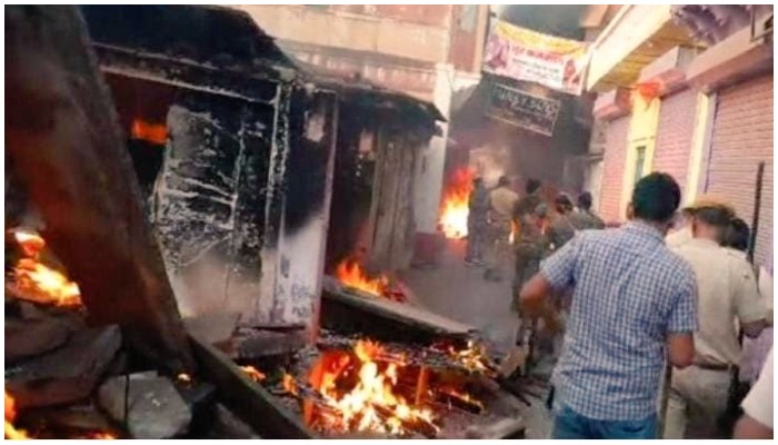 People and cops pass through the shops engulfed in flames in Karauli, Rajasthan. — Twitter.