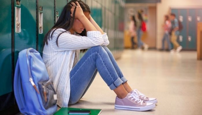 Frustrated Asian teenage young woman female student with head in hands in hallway in school. Unsplash