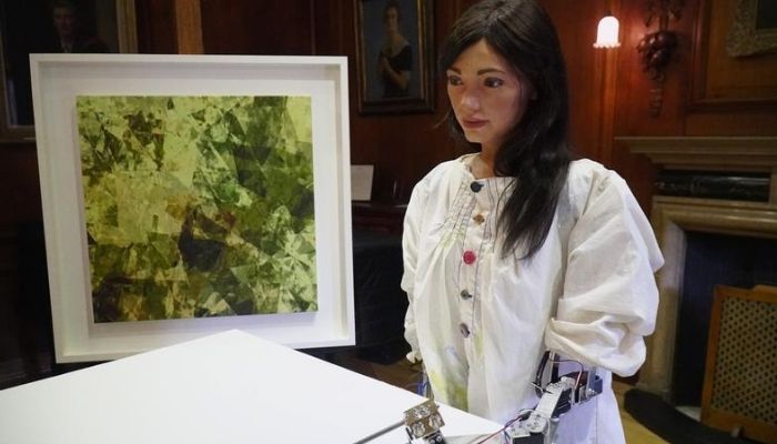 Robot artist Ai-Da sketches using a pencil attached to her robotic arm, while standing next to a painting based on her computer vision data when run through algorithms developed by computer scientists in Oxford, Britain June 4, 2019. Reuters