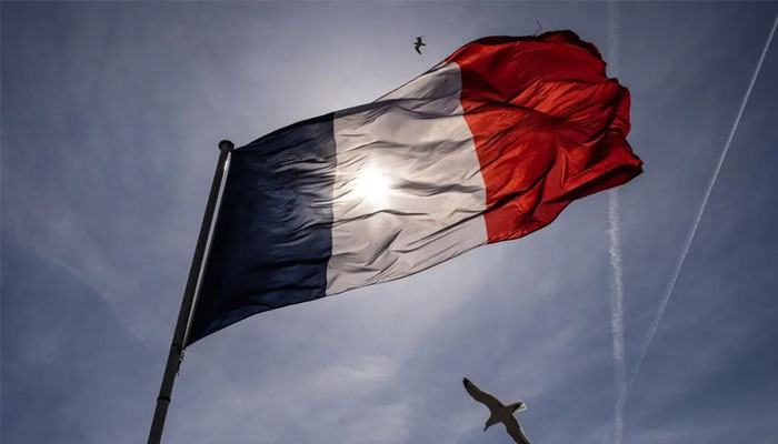 A picture taken on April 10, 2022 shows the sun shining through a French national flag in the Mont Saint-Michel. (Reuters)