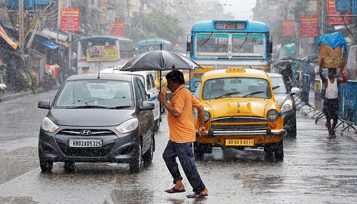 A man carrying an umbrella runs as he crosses a busy road during rain in Kolkata, India, on July 10, 2018. — Reuters