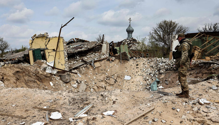 A Ukranian serviceman looks into a crater and a destroyed home are pictured in the village of Yatskivka, eastern Ukraine on April 16, 2022. — AFP