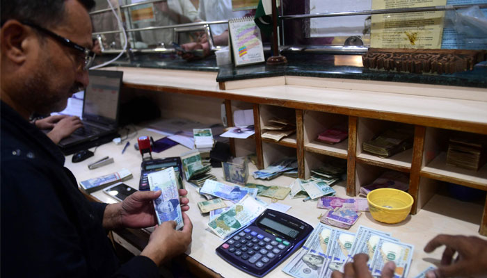 A currency dealer can be seen counting Pakistani and US currency notes. — AFP/File