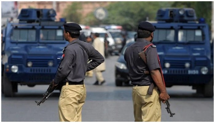 Two armed cops stand on a road with police vans in the background.— AFP/File