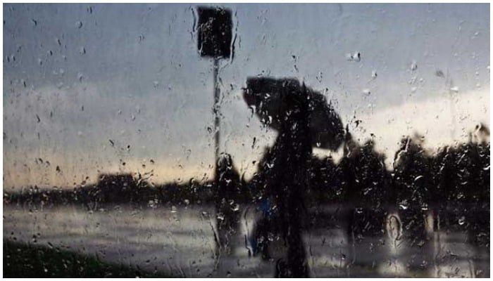Man stands under an umbrella behind a wet glass screen. — AFP/ file