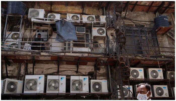 A man uses his mobile phone as he sits amidst the outer units of air conditioners, at the rear of a commercial building in New Delhi, India, April 30, 2022.— Reuters