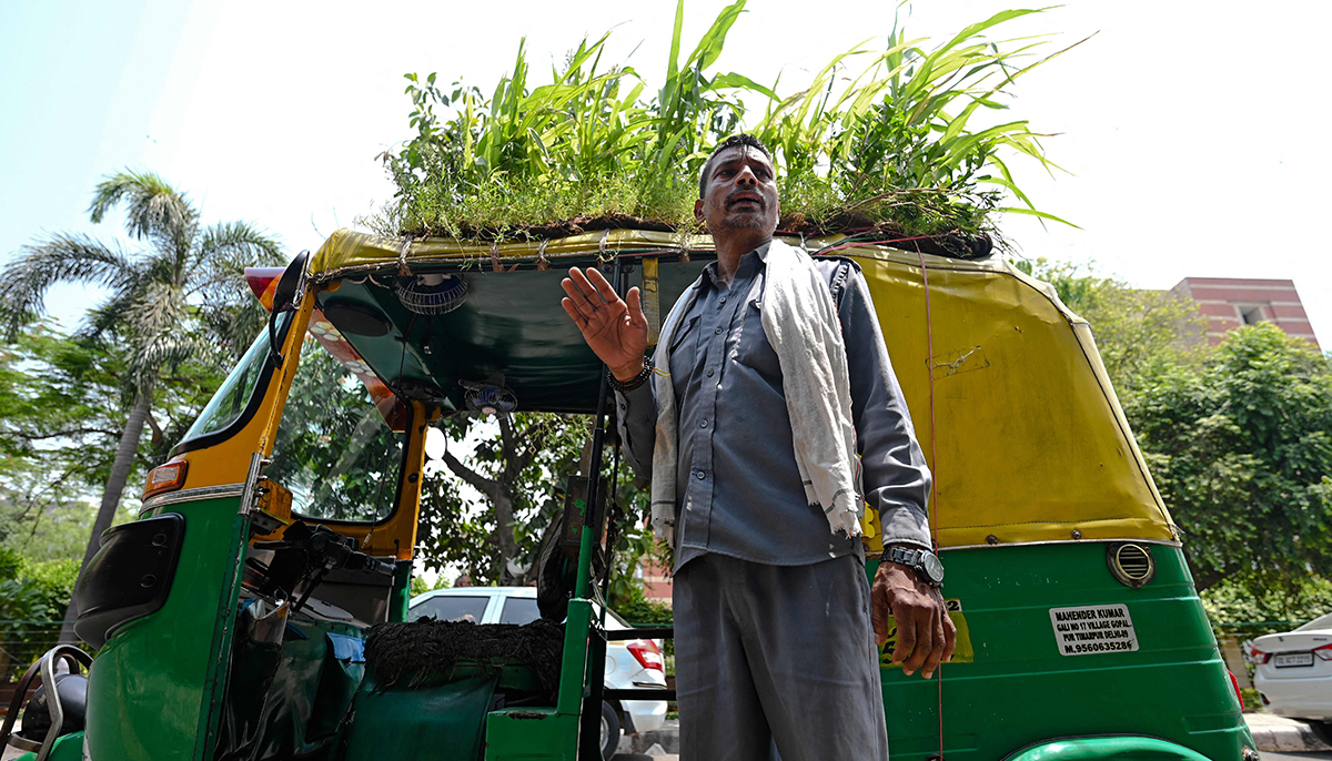Autorickshaw driver Mahender Kumar stands beside his vehicle with a garden on its roof, in New Delhi on May 2, 2022. — AFP