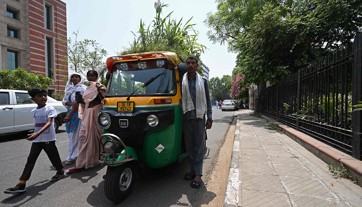 Pedestrians walk past as autorickshaw driver Mahender Kumar stands beside his vehicle with a garden on its roof, in New Delhi on May 2, 2022. — AFP