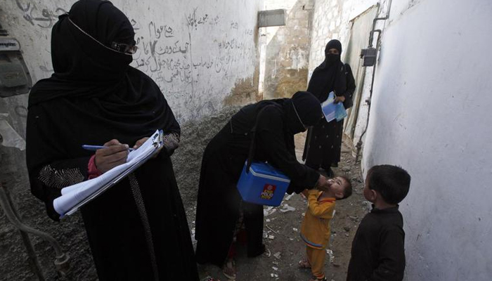 A polio vaccinator (2nd L) administers polio vaccine drops to a boy while a colleague takes notes nearby, along a street in a Karachi slum October 20, 2014. — Reuters
