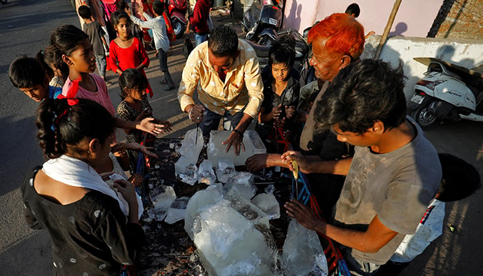 28 اپریل 2022 کو بھارت کے احمد آباد میں گرم موسم کے دوران ایک شخص کچی بستی کے مکینوں میں تقسیم کرنے کے لیے برف کا ایک بلاک توڑ رہا ہے۔ - رائٹرز