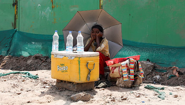 A girl selling water uses an umbrella to protect herself from the sun as she waits for customers on a hot summer day, in New Delhi, India, on April 27, 2022. — Reuters