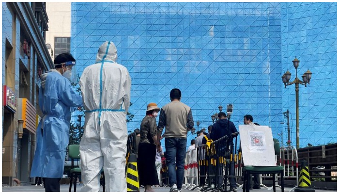 Workers in protective suits stand next to people lining up a makeshift nucleic acid testing site during a mass testing for the coronavirus disease (COVID-19) in Chaoyang district of Beijing, China May 4, 2022. — Reuters