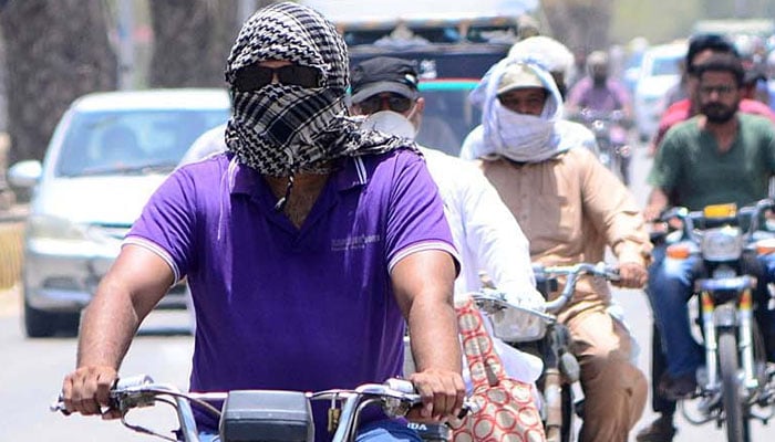 A motorcyclist on the way while covering their faces with cloth to protect from heat stroke during extreme heatwave. Photo—APP/ Farhan Khan