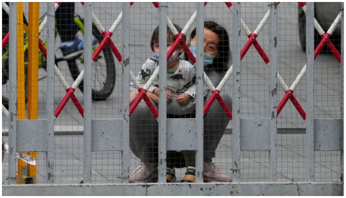 A resident and a child look out through gaps in the barriers at a closed residential area during lockdown, amid the coronavirus disease (COVID-19) pandemic, in Shanghai, China, May 10, 2022. — Reuters