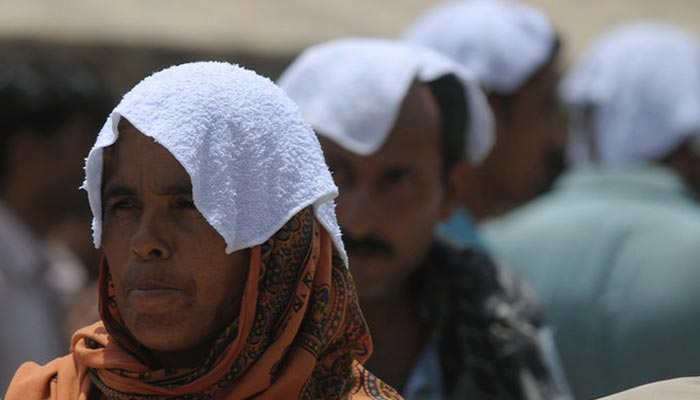 Pakistani relatives of heatstroke victims, their heads covered with wet towels, wait outside a hospital during a heatwave in Karachi on June 29, 2015. — AFP/File