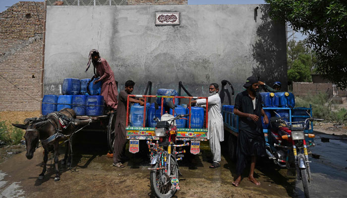 11 مئی 2022 کو لی گئی اس تصویر میں، پاکستان کے جنوبی صوبہ سندھ میں واقع جیکب آباد کے گرم ترین شہر میں گرمی کی لہر کے دوران فروخت کرنے والے واٹر سپلائی پلانٹ سے دکاندار اپنی گدھا گاڑیوں پر پینے کے پانی سے کین بھر رہے ہیں۔  - اے ایف پی