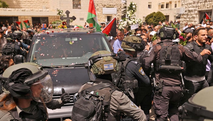 Israeli security forces surround a vehicle carrying the casket of slain Al-Jazeera journalist Shireen Abu Akle out of a hospital, as Palestinian mourners toss rose petals, before being transported to a church and then her resting place, in Jerusalem, on May 13, 2022. — AFP