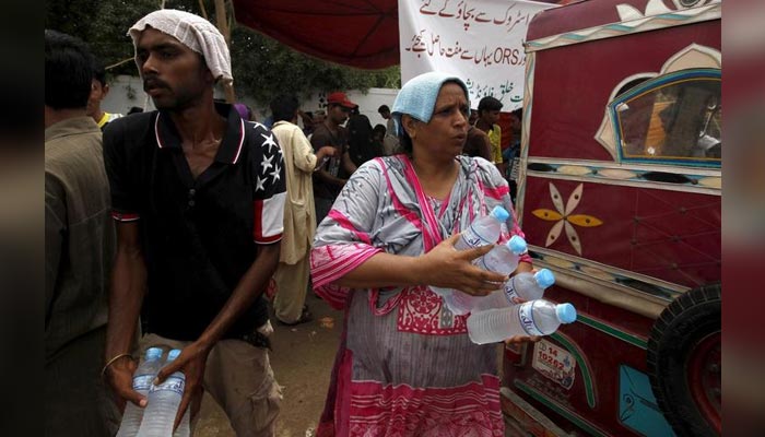 Volunteers cover their heads with water-soaked towels, to beat the heat, while distributing water bottles, outside Jinnah Postgraduate Medical Centre (JPMC) in Karachi, Pakistan, June 25, 2015 — Reuters/File