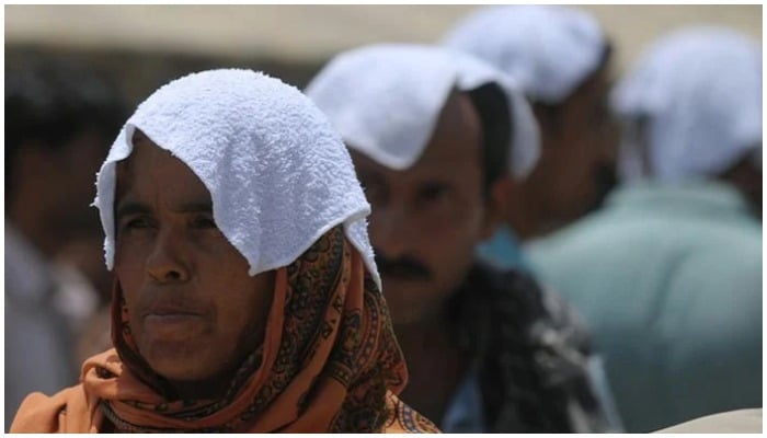 Pakistani relatives of heatstroke victims, their heads covered with wet towels, wait outside a hospital during a heatwave in Karachi on June 29, 2015. — AFP/File