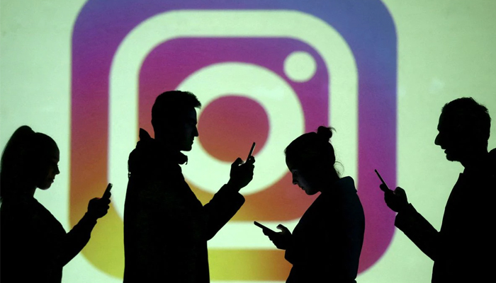 Silhouettes of mobile users are seen next to a screen projection of Instagram logo in this picture. Photo—REUTERS/Dado Ruvic/Illustration