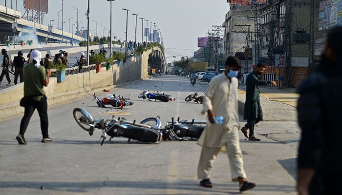 People walk past motorbikes that were damaged during a clash between protestors and police in Rawalpindi on May 25, 2022, as all roads leading into Pakistans capital were blocked ahead of a major protest planned by ousted prime minister Imran Khan and his supporters. — AFP
