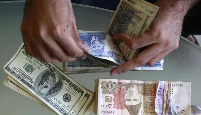 A man counts Pakistani rupee notes with stacks of dollar bills and rupee notes lying on the table. — Reuters/File