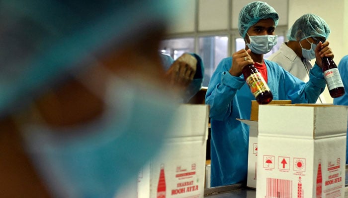 In this photograph taken on May 21, 2022, employees pack bottles of Rooh Afza beverages in cardboard boxes at the end of the assembly line at Hamdard Laboratories (India) factory in Manesar. — AFP