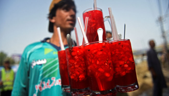 In this photograph taken on May 25, 2022, a vendor prepares to serve Rooh Afza watermelon beverages to customers along a roadside stall in Karachi. — AFP