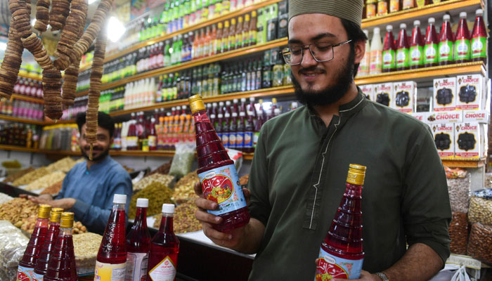 28 اپریل 2022 کو لی گئی اس تصویر میں، کراچی کے ایک بازار میں ایک دکاندار روح افزا مشروبات کی بوتلیں گاہکوں کو دکھا رہا ہے۔— اے ایف پی