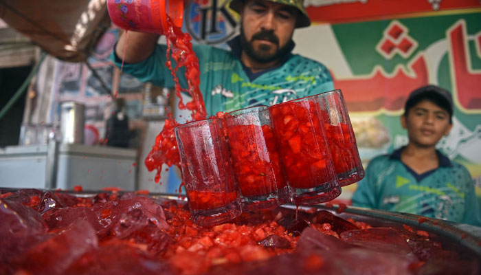 25 مئی 2022 کو لی گئی اس تصویر میں، ایک دکاندار کراچی میں سڑک کے کنارے ایک اسٹال کے ساتھ صارفین کو روح افزا تربوز کے مشروبات پیش کرنے کی تیاری کر رہا ہے۔  - اے ایف پی