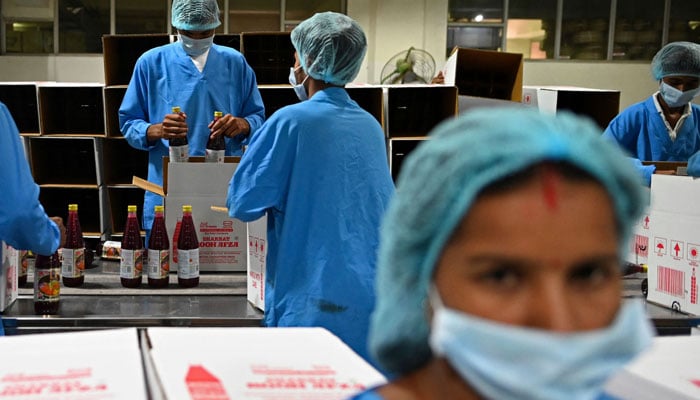 In this photograph taken on May 21, 2022, employees pack bottles of Rooh Afza beverages in cardboard boxes at the end of the assembly line at Hamdard Laboratories (India) factory in Manesar. — AFP