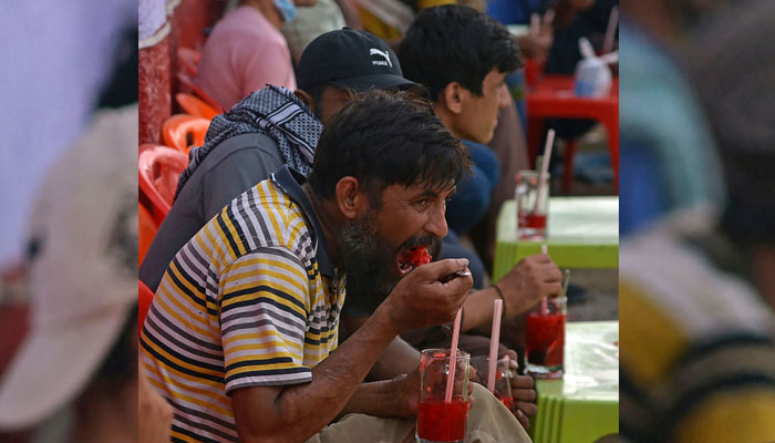 25 مئی 2022 کو لی گئی اس تصویر میں، لوگ کراچی میں سڑک کے کنارے ایک اسٹال پر روح افزا تربوز کے مشروبات پی رہے ہیں۔  - اے ایف پی