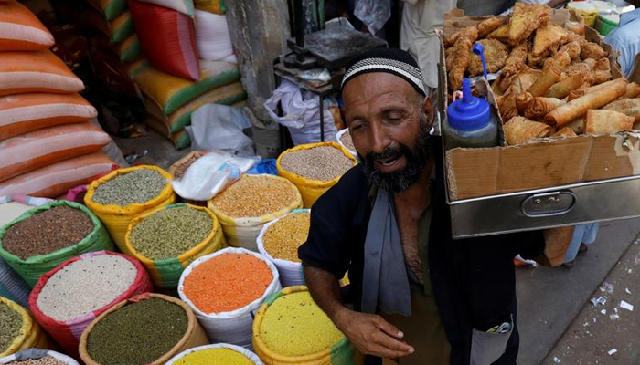 A vendor with a pane of vegetable rolls and samosas, a traditional snack, walks past the sacks of grain and lentils at a wholesale market in Karachi, Pakistan April 2, 2019. — Reuters