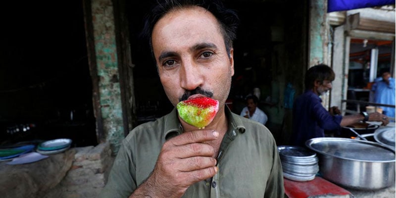 جیکب آباد، پاکستان، 16 مئی، 2022 میں ایک کیفے کے باہر ٹھنڈا ہونے کے لیے ایک شخص گولا گانڈا کھا رہا ہے، جب وہ منڈوا ہوا برف کا میٹھا کھا رہا ہے۔ تصویر: رائٹرز
