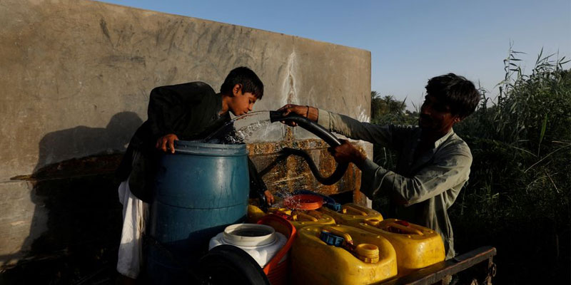 ایک باپ اور اس کا بیٹا 15 مئی 2022 کو پاکستان کے جیکب آباد کے رہائشی علاقے میں ہیٹ ویو کے دوران گھر گھر فروخت کرنے کے لیے ایک نجی پمپ سے پانی کے کنستر بھر رہے ہیں۔ تصویر: رائٹرز