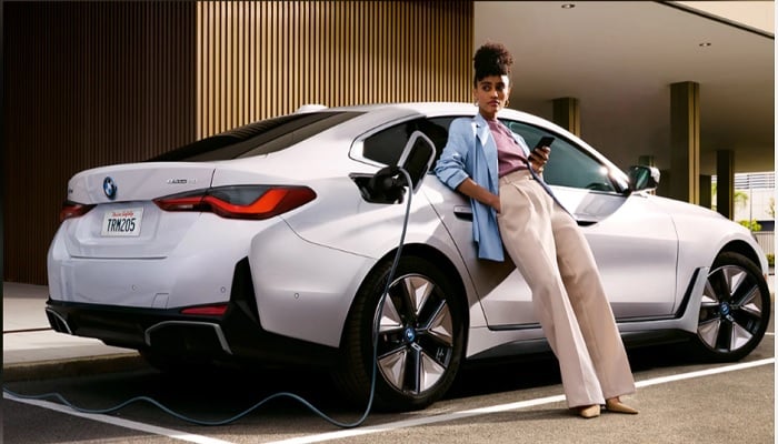 A woman leans against BMW electric car while it is being recharged.— bmwusa.com