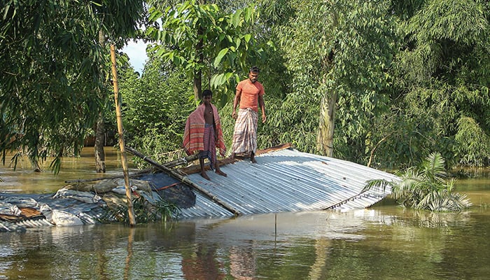 Flood-affected people stand on the roof of their collapsed house in a flooded area following heavy monsoon rainfalls in Sunamganj on June 21, 2022. — AFP