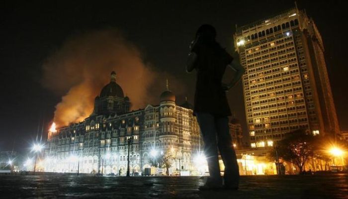 A reporter talks on her phone as smoke is seen coming from Taj Hotel in Mumbai, November 27, 2008 — Reuters