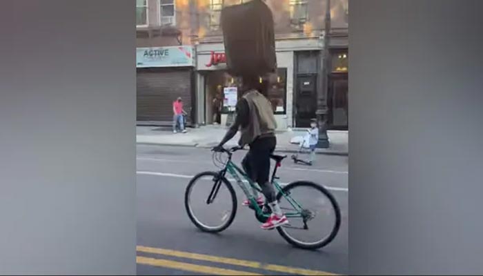 Pria dengan sempurna menyeimbangkan koper di kepala saat bersepeda