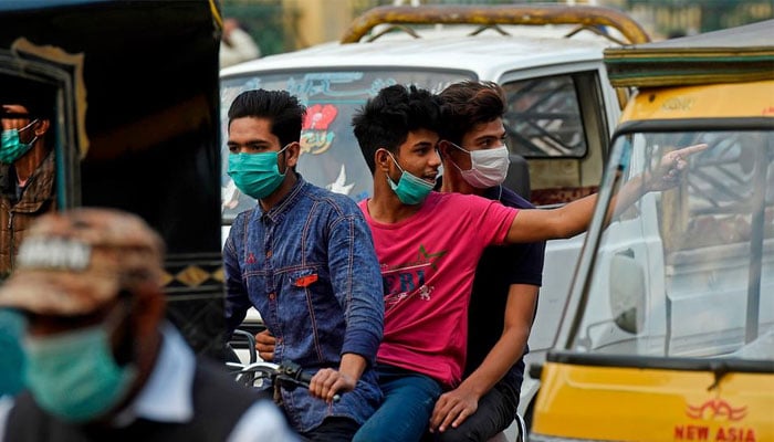 Three youngsters wearing masks pillion ride a motorcycle on a busy road in Pakistan. — AFP/File