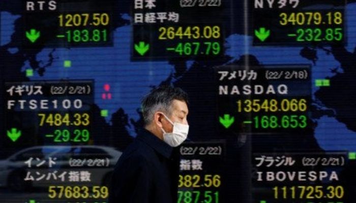 A man wearing a mask walks past an electronic board displaying Japans Nikkei index and other countries stock market index prices in Tokyo, Japan, on February 22, 2022 — Reuters