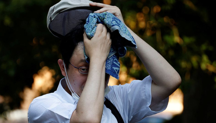 ٹوکیو، جاپان، 30 جون، 2022 میں 1875 کے بعد سے ٹوکیو کی گرم ترین جون کی لکیر کے نیچے ایک پارک میں ایک آدمی تولیہ سے پسینہ پونچھ رہا ہے۔ — رائٹرز