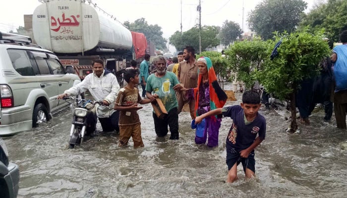 People stand in rainwater on a Karachi road while traffic is blocked in this PPI file photo.