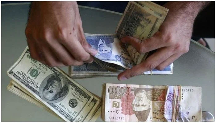 A man counts Pakistani rupee notes with stacks of dollar bills and rupee notes lying on the table. — Reuters/ File