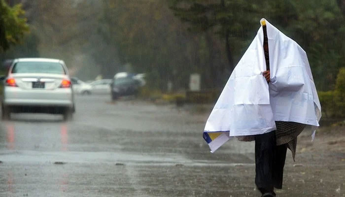 A man walks on a road while covering himself with a sheet during a rainy day. — AFP/File